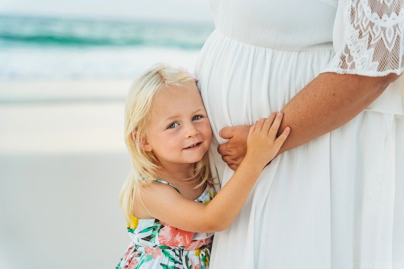 Little kid hugging mum’s pregnant belly, beach photoshoot