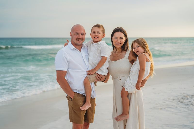 Family of four wearing coordinated white, cream, and tan outfits during a beach photo session in Destin, Florida