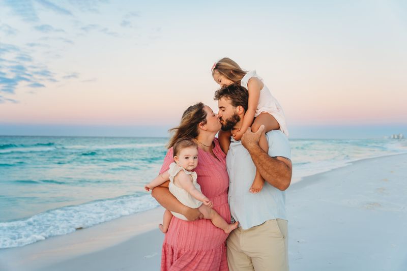 Family of four wearing dusty pink, light blue, and white outfits during a sunset beach photoshoot in Destin, Florida