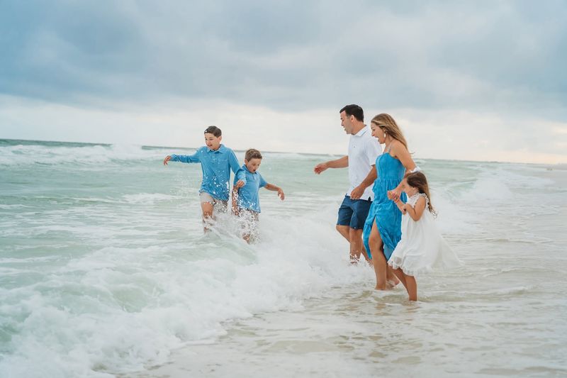 Family of five in coordinated blue and white outfits playing in the Gulf waves during their Destin beach photo session