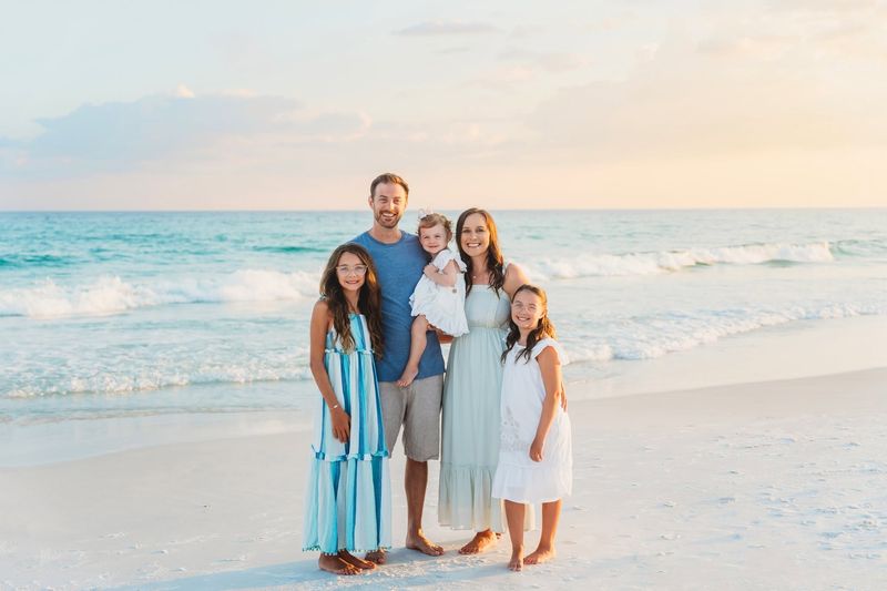 Family of five wearing coordinated blue and white beach outfits, including a striped dress, during a Destin family photo session