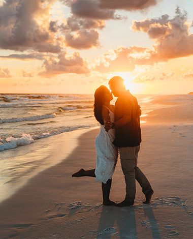 a couple dancing on a beach, setting sun in the background