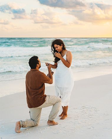 guy is proposing to his girlfriends on a beach, standing on one knee