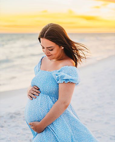 sunset maternity shoot, woman in blue dress looking at her belly